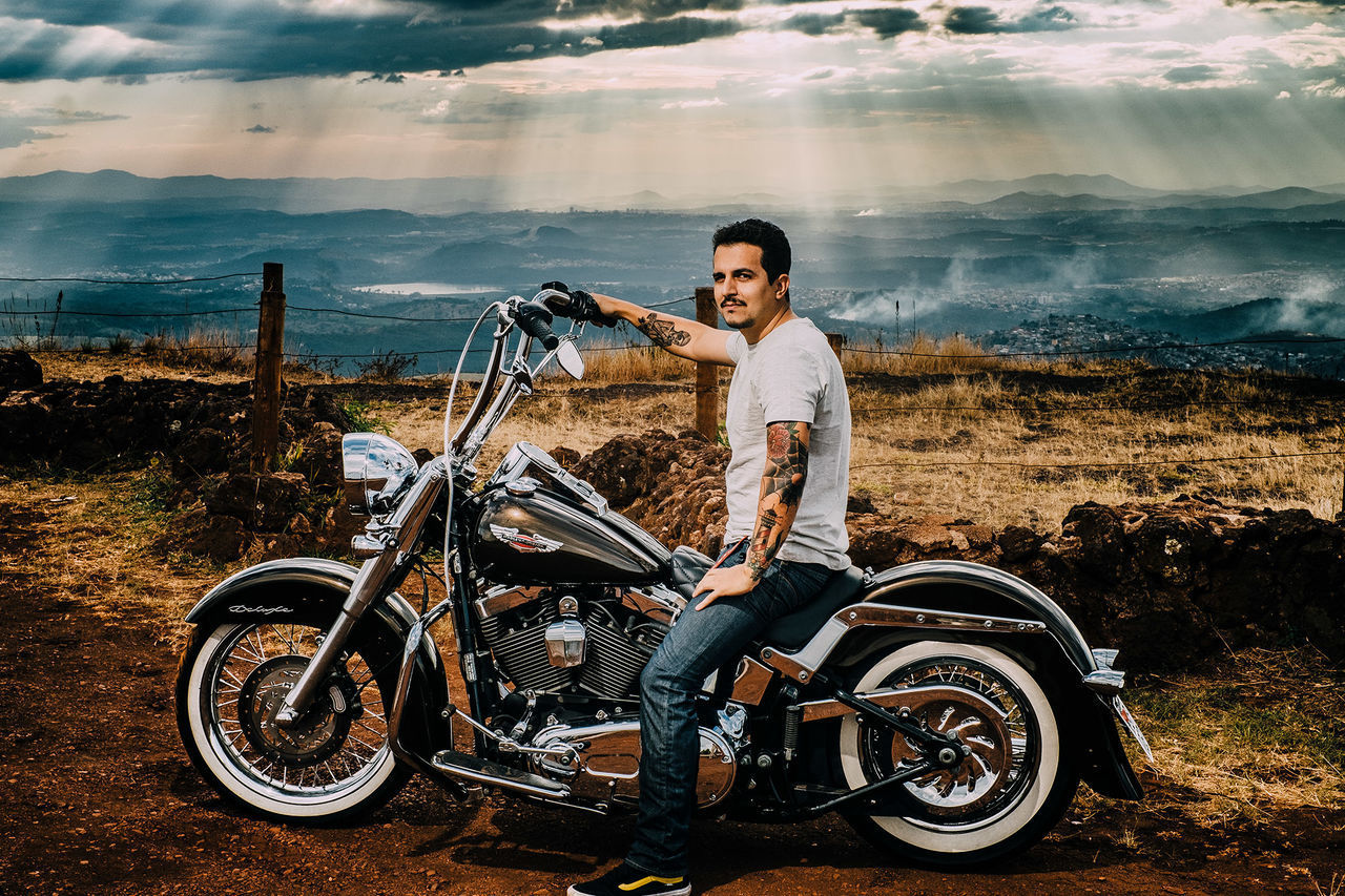 FULL LENGTH OF YOUNG MAN SITTING ON MOTORCYCLE AGAINST SKY