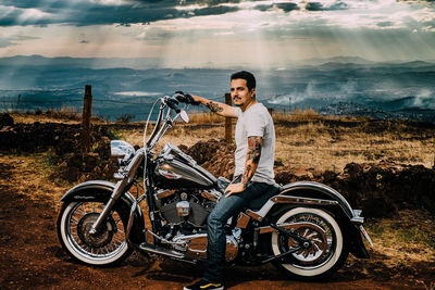 Young man sitting on motorcycle against sky