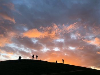 Silhouette people standing on mountain against cloudy sky during sunset