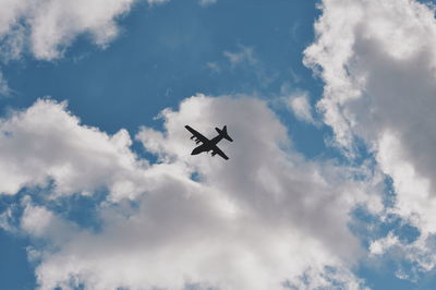 Low angle view of silhouette airplane flying against cloudy sky