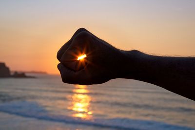 Optical illusion of hand holding sun at sea during sunset