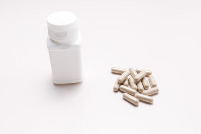 Close-up of pills spilling from bottle against white background