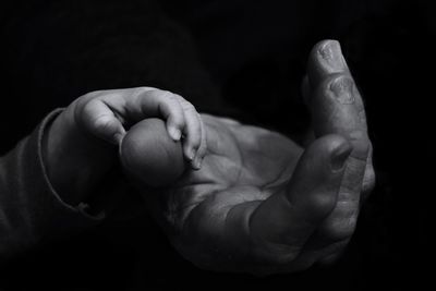 Cropped hands of father and baby against black background