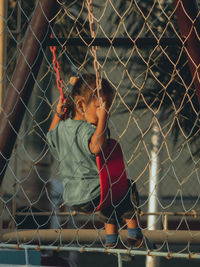 Girl looking through chainlink fence in field