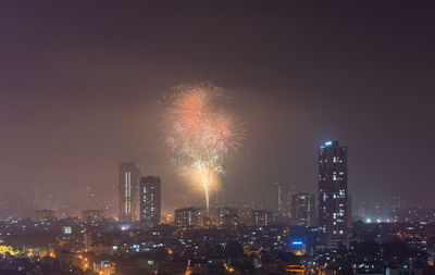 Firework display in city against sky at night