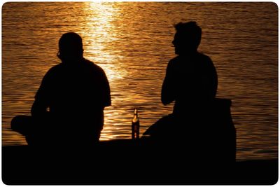 Silhouette people standing by river at sunset