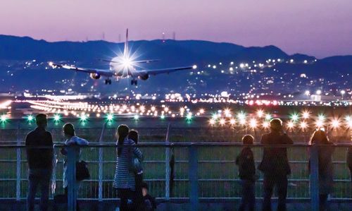 People standing by railing against illuminated cityscape at night