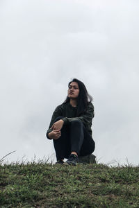 Young woman sitting on field against sky