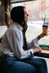 Smiling brunette girl by the window in a cafe drinking a coffee