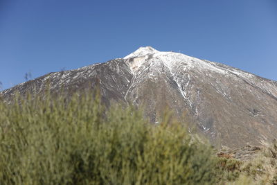 Low angle view of snowcapped mountain against clear blue sky