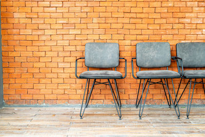 Empty chairs on sidewalk against brick wall