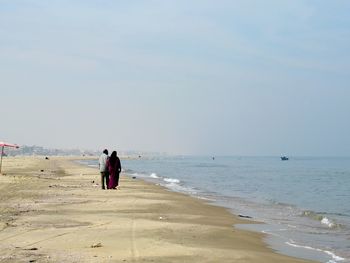 Rear view of people at beach against sky