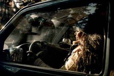 Side view of happy young woman driving off-road vehicle seen through glass