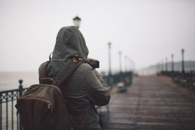 Rear view of person wearing hood photographing jetty