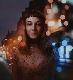 Portrait of young woman looking at illuminated city