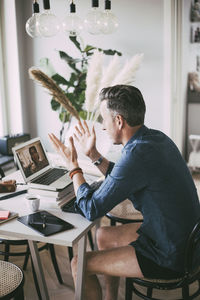 Side view of young man using mobile phone while sitting on table