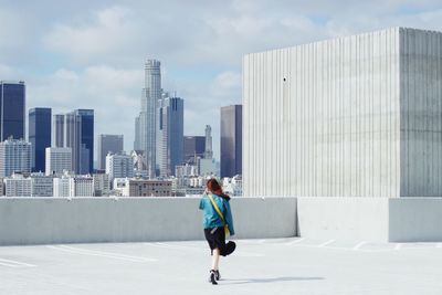 Rear view of woman walking by modern buildings against sky