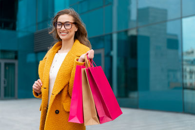 Portrait of smiling woman holding shopping bag while standing outdoors