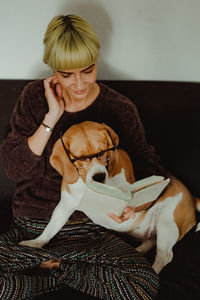 Woman with dog reading book while sitting on sofa