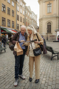 Full length of senior tourist couple reading map together in city