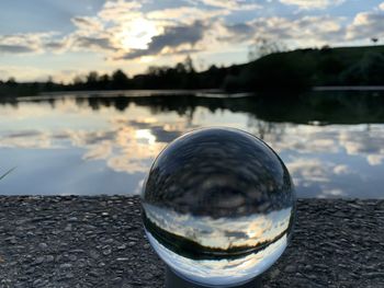 Close-up of crystal ball against lake during sunset