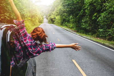 Woman walking on road by trees in city