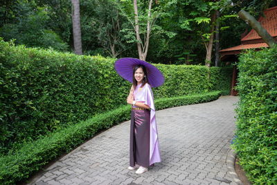 Portrait of woman holding umbrella while standing on footpath amidst trees