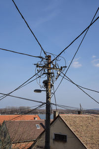 Low angle view of telephone pole by building against sky