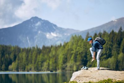 Hiker standing on rock formation by lake against mountain