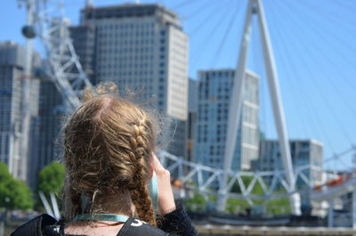 Rear view of woman looking at ferris wheel in city