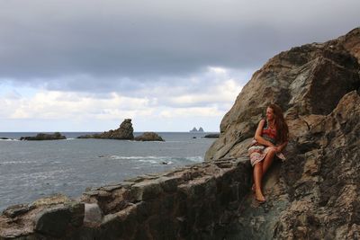 Woman standing on cliff by sea against sky