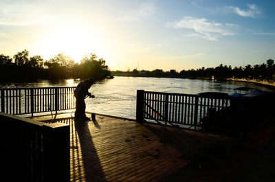 Silhouette woman standing on jetty by river against sky