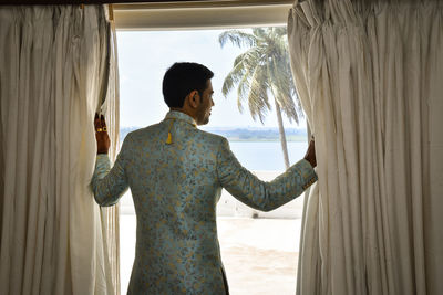 Rear view of man standing by window