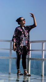 Woman shielding eyes while standing by railing against sea clear sky 