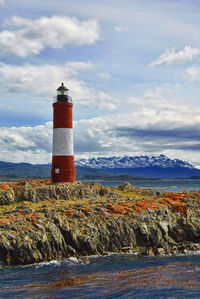 Lighthouse on sea against cloudy sky