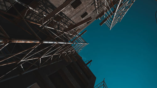 Low angle view of crane against building against clear blue sky