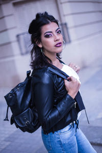 Portrait of woman with backpack standing against building