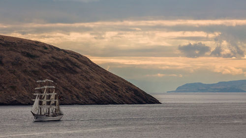 Ship sailing in sea by mountains against sky during sunset