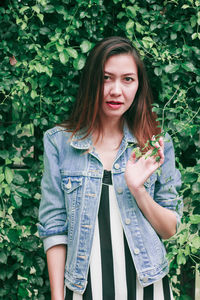 Portrait of beautiful young woman standing against plants