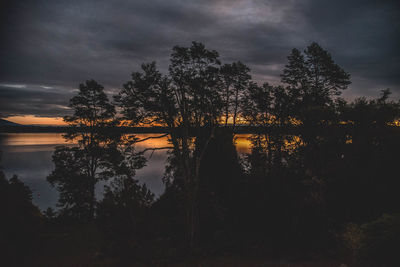 Silhouette trees by lake against sky at sunset