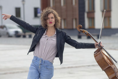 Portrait of smiling woman holding violin while dancing on street