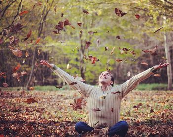 Autumn leaves falling on smiling young man sitting on field