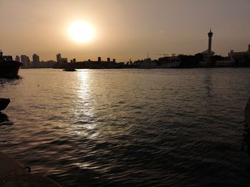 Silhouette buildings by sea against sky during sunset