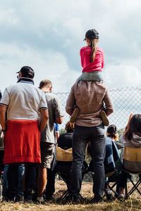 People standing by fence on ground against sky