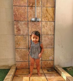 Portrait of girl taking shower while standing against wall