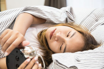 Woman holding alarm clock while lying down on bed