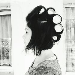 Side view of woman with hair curler at home