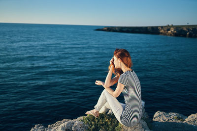 Woman sitting on rock by sea against sky