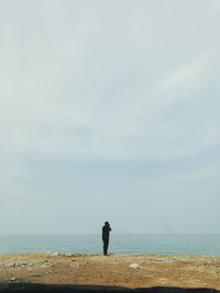 Rear view of man standing at beach against sky