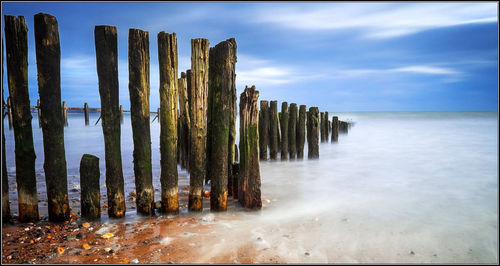 Wooden posts in sea against sky